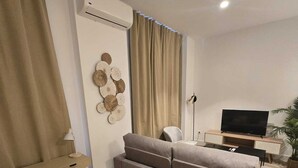 Een moderne woonkamer met een bank, een bureau met stoel, een televisie en een decoratief wandobject.