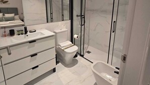 Een moderne badkamer met een grote spiegel, een toilet, een bidet en een bad.