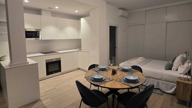 Een moderne, compacte leefruimte met een eethoek, kitchenette en een bed.