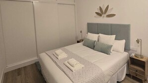 Een moderne slaapkamer met een groot bed, een hoofdbord met een bladmotief en een nachtkastje met een lamp.