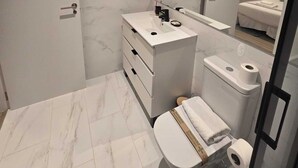 Een moderne badkamer met een marmeren vloer, een witte wastafel met wastafel, toilet en een douchegedeelte.