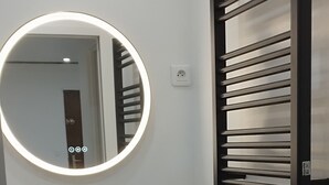 Une salle de bain avec un meuble-lavabo noir, un miroir rond avec un éclairage intégré, un porte-serviettes noir et un sol en marbre.