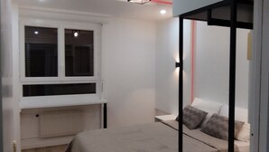 Une chambre avec une fenêtre, un radiateur, un lit avec des oreillers et un luminaire fixé au mur.