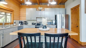 Una cocina moderna con vigas de madera, una isla central con sillas, electrodomésticos de acero inoxidable y una planta decorativa.