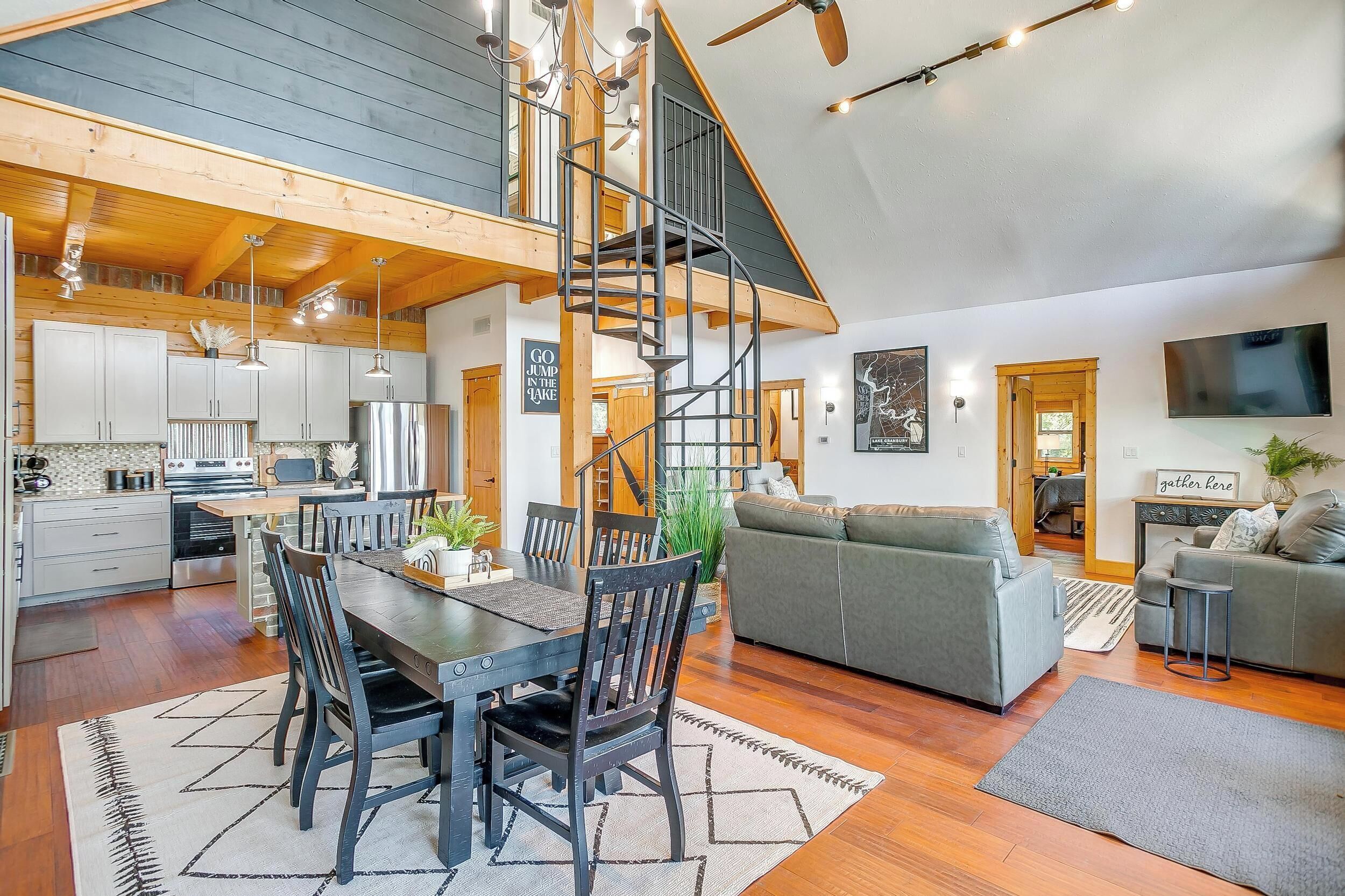 A spacious living area with a dining table, sofa, and staircase connecting to a loft.