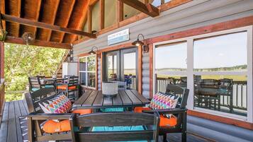 Un espace extérieur aménagé avec des tables et des chaises en bois, protégé par un auvent, une enseigne indiquant « Bienvenue au bord du lac », et de grandes fenêtres offrant une vue sur le lac.