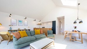 A spacious living area with a sofa, a dining table, and a kitchen area. - Woodlark -  Luxury Cottages (Bradworthy)