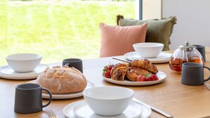 A breakfast setting with a table, bread, pastries, and a teapot. - Woodlark -  Luxury Cottages (Bradworthy)