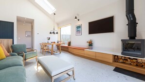 A modern living room with a sofa, a dining table, and a fireplace. - Woodlark -  Luxury Cottages (Bradworthy)