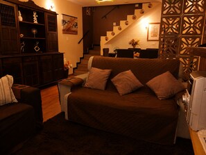 Una sala de estar acogedora con un sofá marrón, un mueble de madera y una escalera que sube.