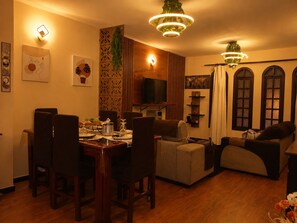 Un comedor con una mesa dispuesta para cuatro personas, un sofá y un televisor al fondo.