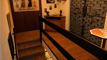 Een trap met een houten leuning en een zwarte balustrade, die leidt naar een ruimte met een bakstenen muur en een bord waarop 'BAR' staat.