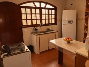 Una cocina compacta con estufa a gas, un lavamanos, refrigerador y una ventana con persianas de madera.