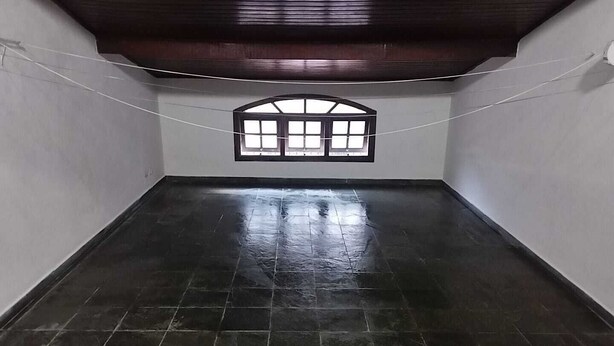 A room with a dark tiled floor, white walls, and a wooden ceiling. There is a window with a black frame and a white curtain.