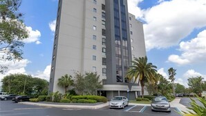 Un hôtel à plusieurs étages, doté d’un design moderne, qui se distingue par une façade verticale en verre, des places de stationnement et un espace verdoyant environnant.