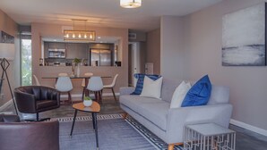 A modern living room with a grey sofa, a coffee table, and a dining area with chairs and a table. - 3BR The Montrose Collective D, Walk to Food & Fun! ★★★★★ (Houston)