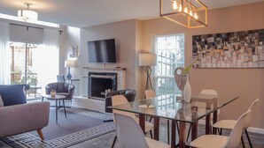 A modern living room with a fireplace, a flat-screen TV, and a dining area with a glass table. - 3BR The Montrose Collective D, Walk to Food & Fun! ★★★★★ (Houston)