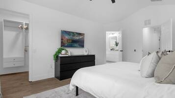 A modern bedroom with a large bed, a dresser, a painting, and a ceiling fan.