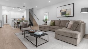 A modern living room with a sectional sofa, a coffee table, and a dining area with chairs and a kitchen in the background.