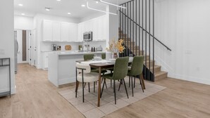 A modern kitchen with white cabinets, a central island, and a dining area with green chairs.