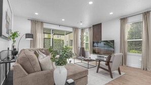 A modern living room with a sofa, coffee table, TV, and a view of greenery outside.