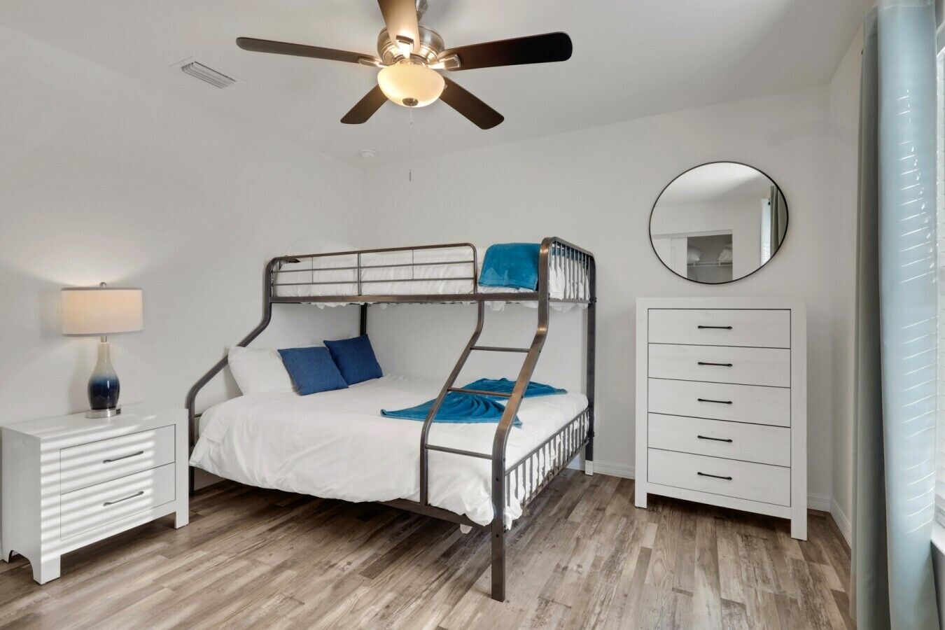 Une chambre avec un lit superposé, un ventilateur de plafond, une lampe de chevet, une commode et un miroir.