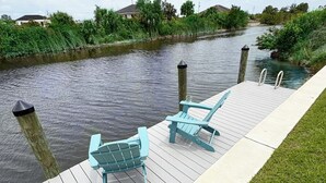 Een steiger met twee Adirondack-stoelen en een betonnen pad langs een rustige rivier.