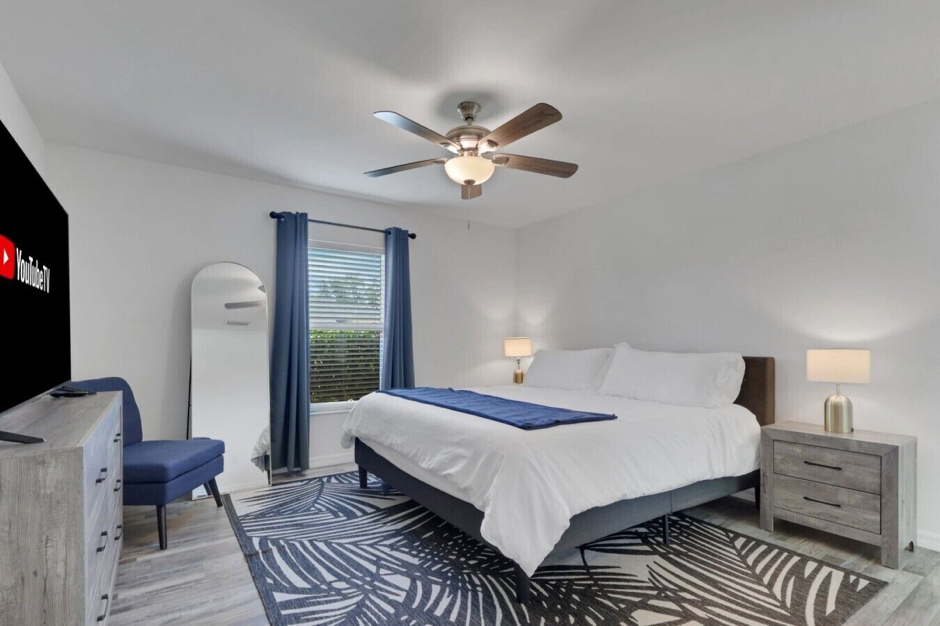 A modern bedroom with a bed, bedside tables, a ceiling fan, a desk, and a window with curtains.