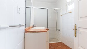 A bathroom with a white sink, a mirror, a shower, and a door with a handle.