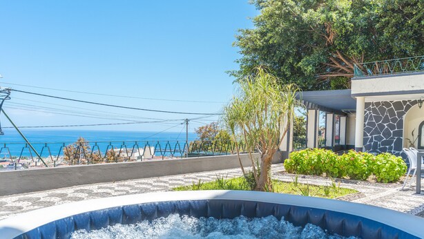 A hot tub with a view of the sea, surrounded by a landscaped garden and a stone building.
