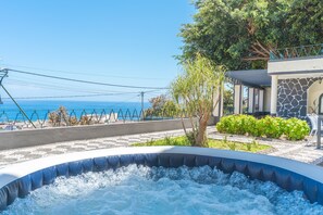 Un jacuzzi con vistas al mar, rodeado de un jardín ajardinado y un edificio de piedra.