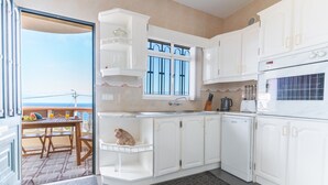 Een keuken met witte kastjes, een raam en uitzicht op zee.