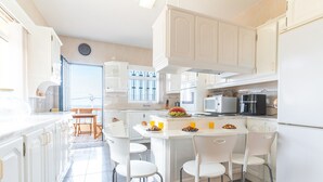 Een lichte keuken met witte kasten, een centraal eiland met stoelen, en uitzicht naar buiten.