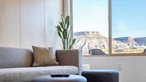 A modern living room with a grey sofa, black ottomans, and a large window offering a view of a canyon.