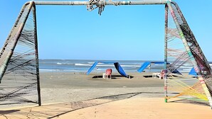 A beach with a large, open structure with blue and white panels, a red chair, and a wooden deck. - Casa de playa a 4 cuadras del mar (Puerto Colombia)