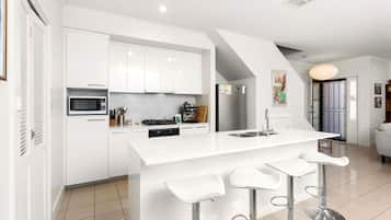 A modern kitchen with white cabinetry, a central island with bar stools, a built-in microwave, and a stainless steel refrigerator.