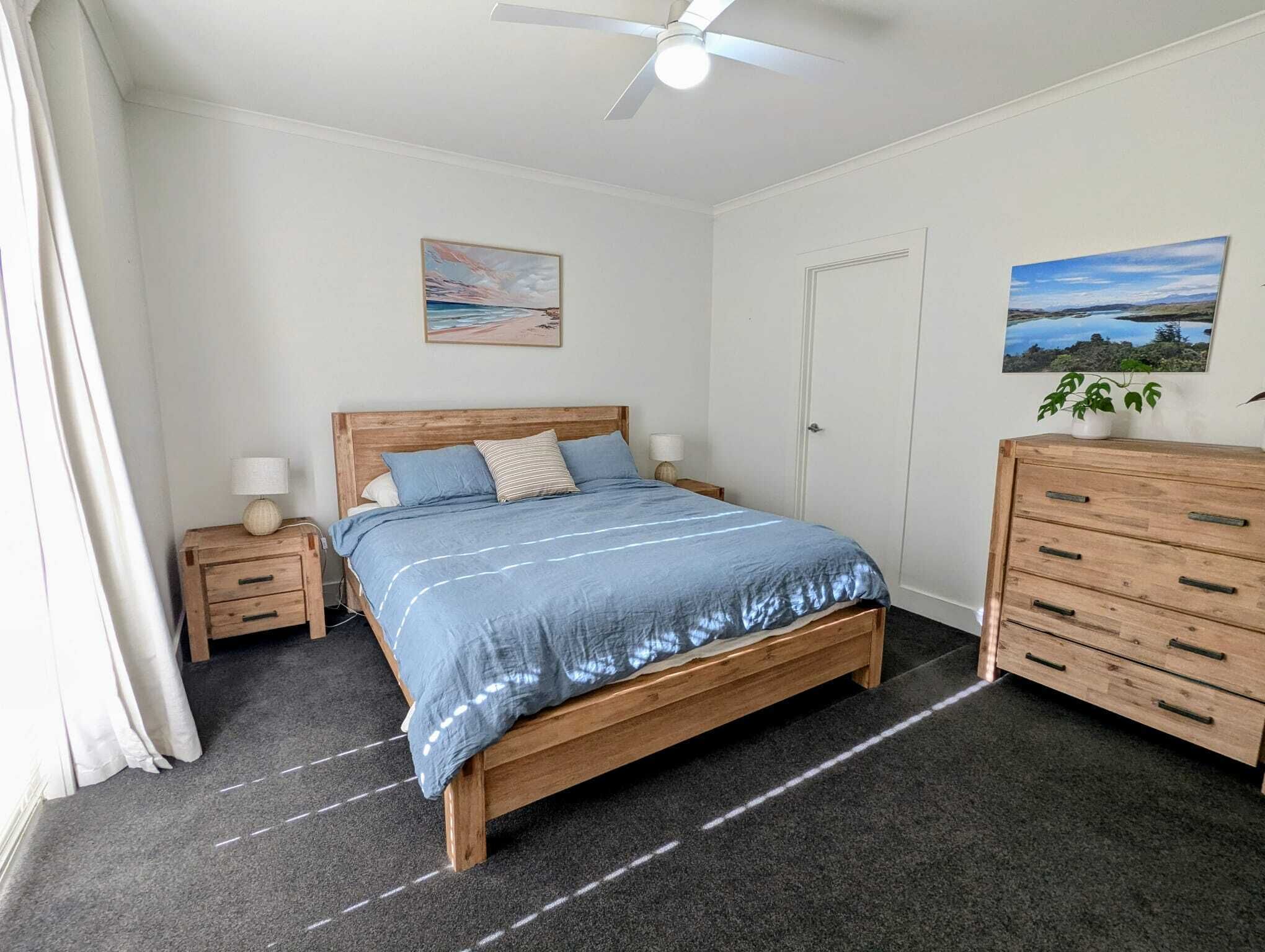 Um quarto com uma cama de madeira, duas mesas de cabeceira, um ventilador de teto e um aparador.