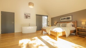 A bedroom with a wooden bed, a large window, a bathtub, and a ceiling light.