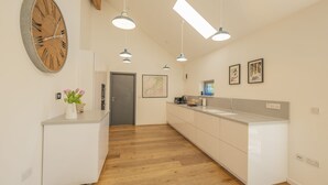 A modern kitchen with a wooden floor, white cabinetry, pendant lighting, and a large wall clock.