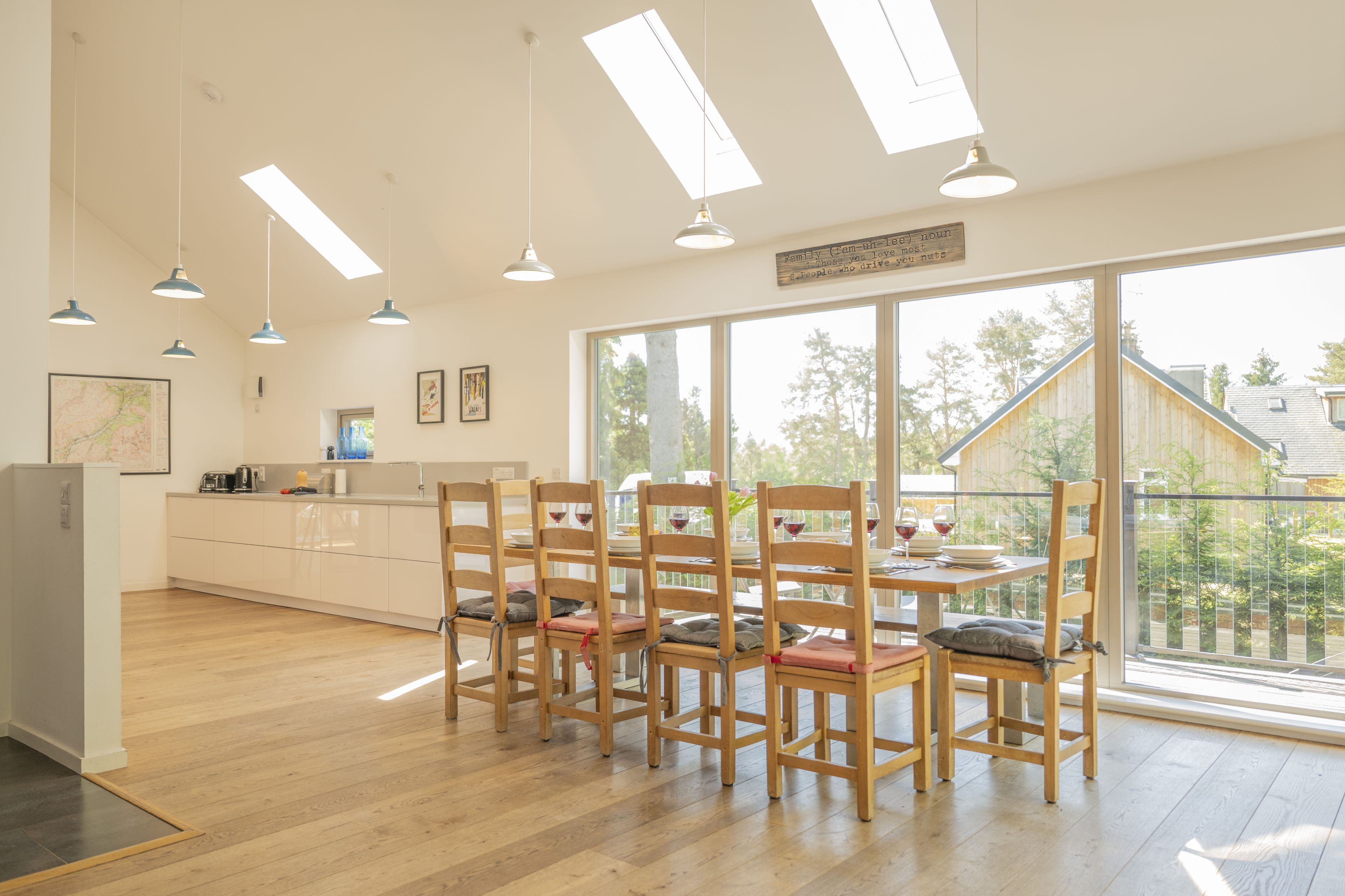 A spacious kitchen with wooden cabinets, a dining area with wooden chairs and a table, and large windows offering a view of the outside.