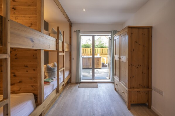 A hallway with wooden bunk beds, a sliding glass door leading to an outdoor area, and a wooden wardrobe. - Sleeps 10 in 1 superking, 1 king and 3 full size bunk beds (6 single beds) (Kingussie)