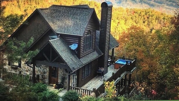 A cabin with a stone foundation, a wooden deck, and a chimney.