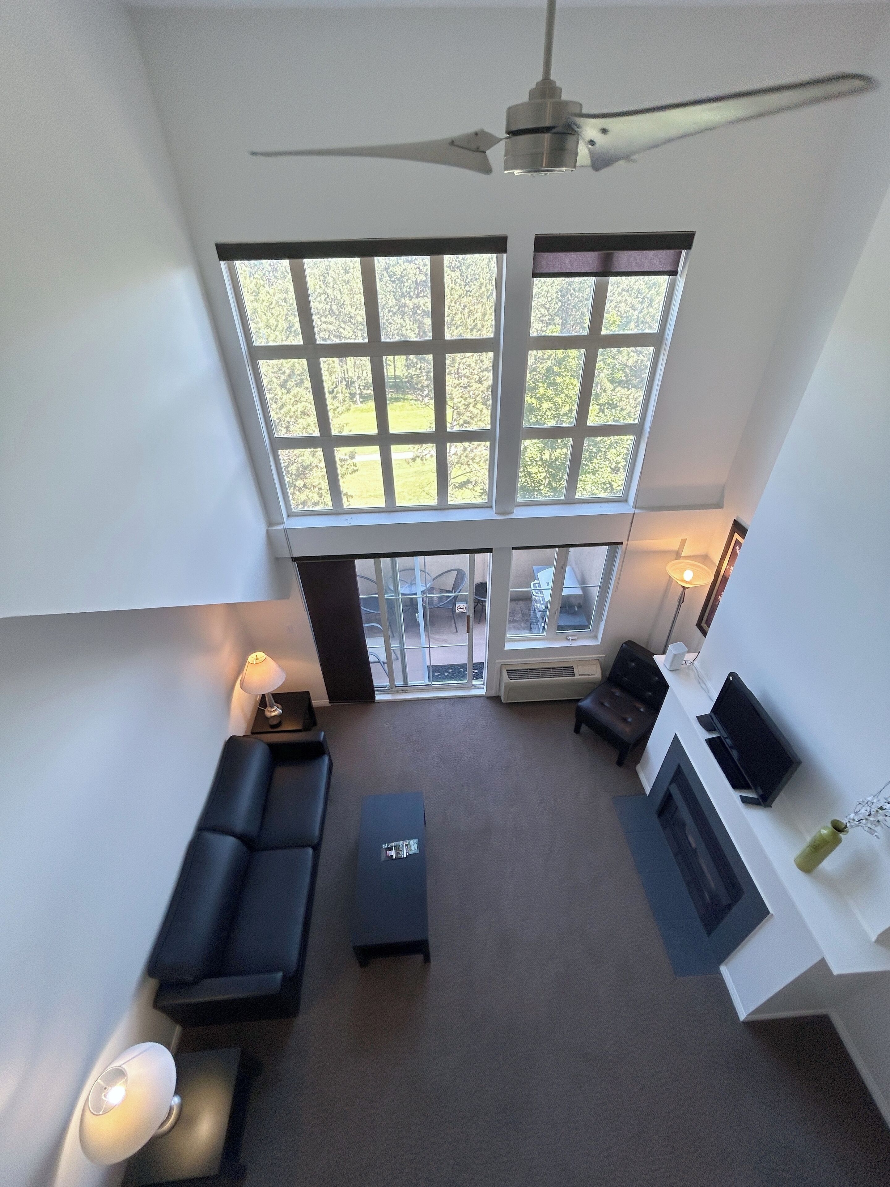 A modern living room with a large window, a ceiling fan, and a fireplace.