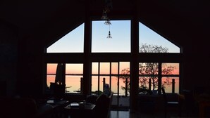 Ein geräumiger Raum mit großen Fenstern und Blick auf ein Gewässer bei Sonnenuntergang.