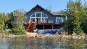 Ein Haus mit einem Steg, einer Holztreppe und mehreren Stühlen am Wasser.
