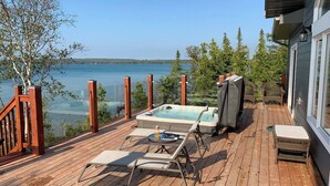Eine Holzterrasse mit Whirlpool, Liegestühlen und einem Tisch mit Getränken.