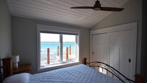 Ein Schlafzimmer mit Bett, einem Fenster mit Meerblick, einem Deckenventilator und einer Tür.