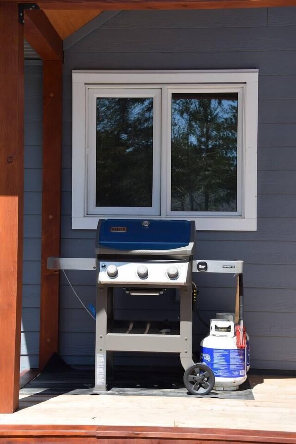 A portable barbecue grill with a propane tank on a wooden deck.