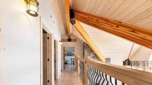 Un interior de madera con techo inclinado, una escalera que conduce a un nivel superior y una barandilla con diseño ondulado.