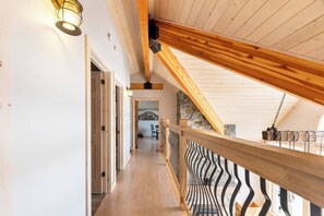 A wooden interior with a sloped ceiling, a staircase leading to an upper level, and a railing with a wavy design.